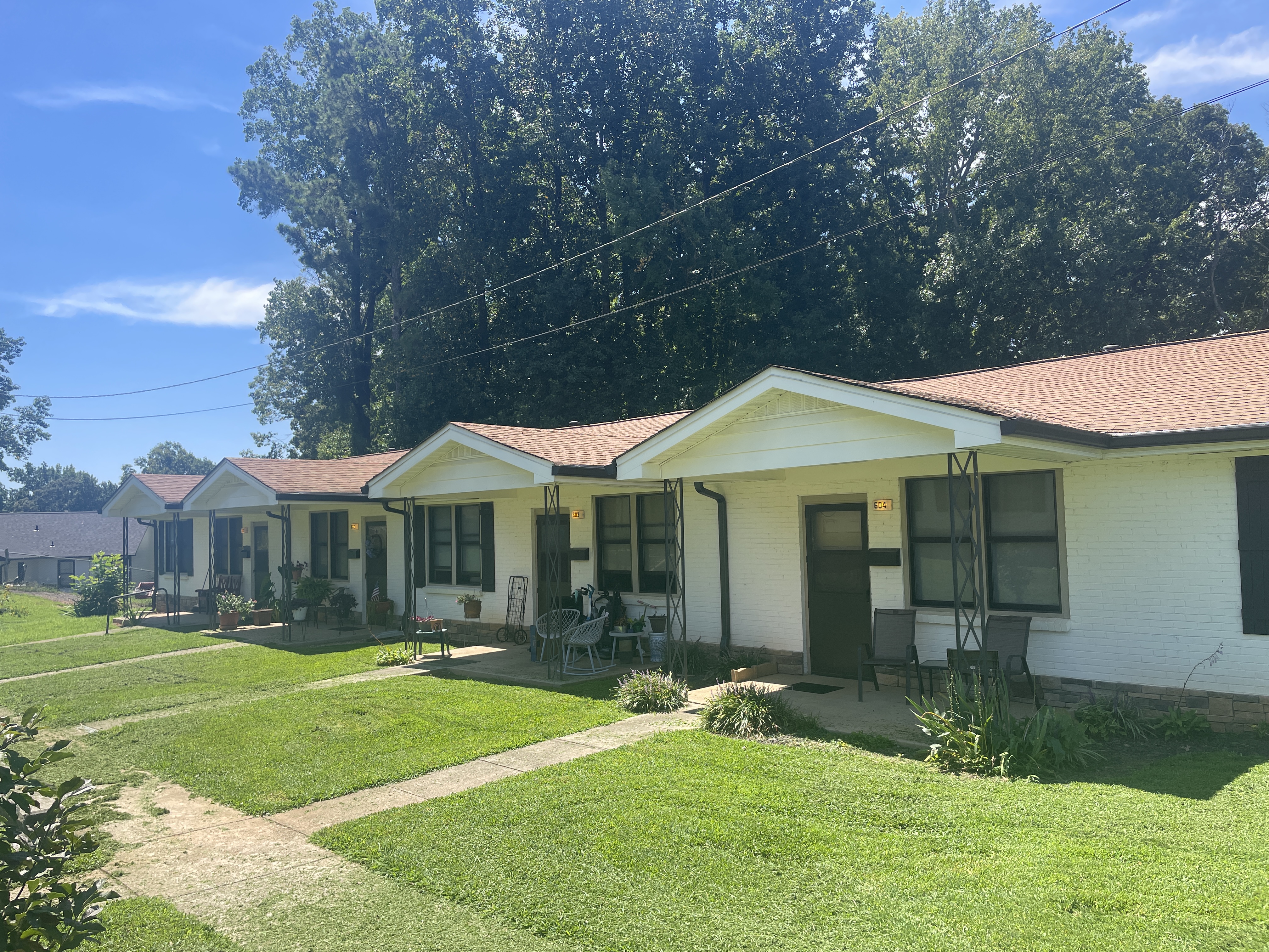Shows a front yard and entrance to a brick row house, contains multiple trees in the front yard
